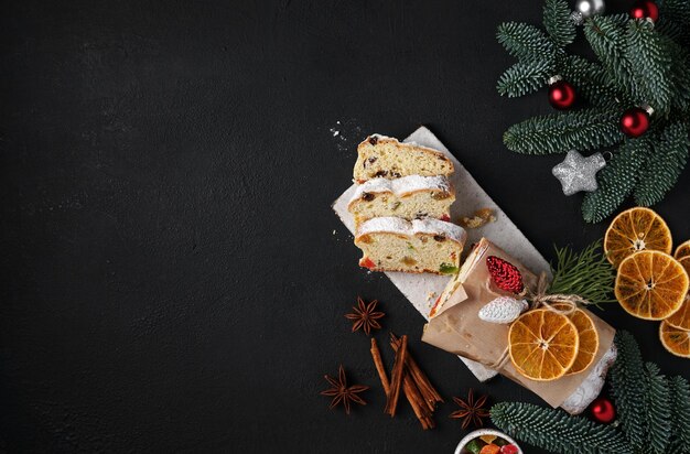 Stollen com frutas em uma mesa escura com decoração de Natal e especiarias, vista superior, espaço para cópia