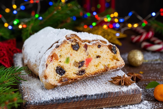 Stollen de Navidad con frutos secos y azúcar en polvo sobre una placa sobre un fondo de madera oscura.