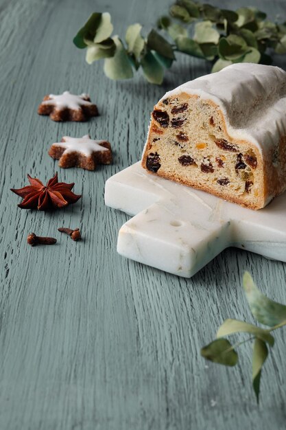 Stollen de Navidad sobre fondo de piedra blanca con eucalipto y guirnaldas de luces de Navidad