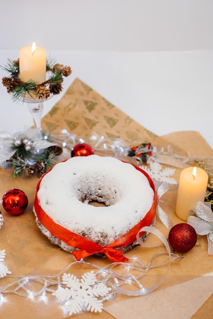 Stollen redondo tradicional de Natal feito de frutas secas e nozes polvilhadas com açúcar de confeiteiro no fundo de uma decoração de Natal com velas. Bolinho de Natal tradicional.