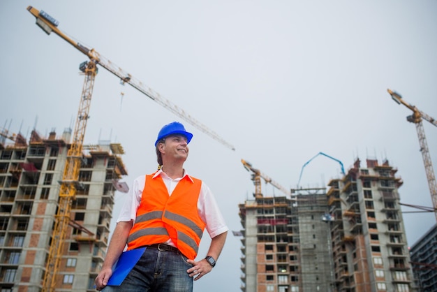 Foto stolzer architekt lächelt auf einer baustelle mit gebäuden und kränen im hintergrund.