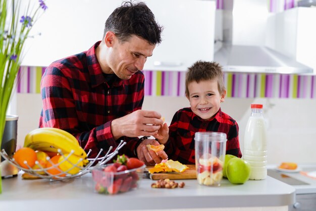 Stolzer junger gut aussehender Vater und sein süßer Sohn zusammen in der Küche, die Smoothie mit frischen Früchten macht. Gesunde Ernährung ist wichtig.