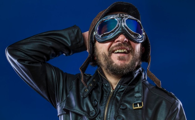 Stolzer Pilot der 20er Jahre mit Sonnenbrille und Vintage-Fliegerhelm. Trägt Lederjacke, Bart und ausdrucksstarke Gesichter