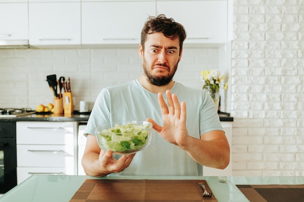 Stop-Diät-Typ sagt bei all seinem Aussehen Grimassen, hält eine Salatschüssel in der Hand