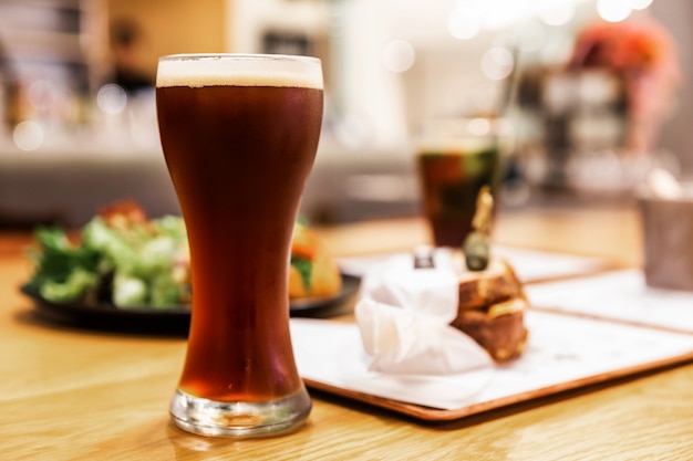 Stout (cerveza negra) con espuma en vaso en una mesa de madera con desenfoque de alimentos