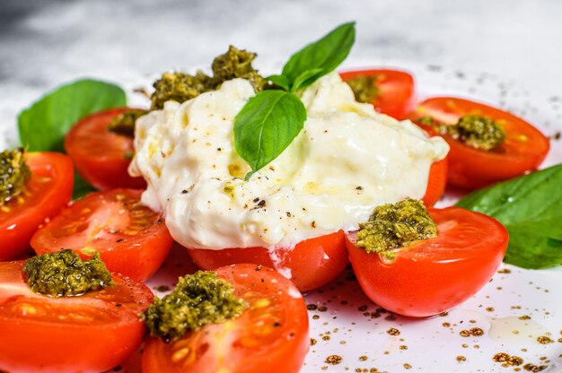 Stracciatella en plato pequeño servido con tomate fresco y albahaca.