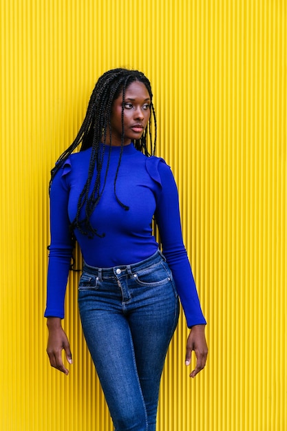 Strahlende afroamerikanische Schönheit, atemberaubende Frau mit blauen Afro-Zöpfen, die vor einer gelben Wand posiert