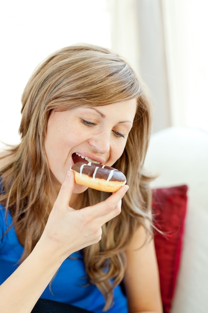 Strahlende Frau isst einen Donut auf einem Sofa