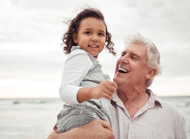 Strand glücklicher und älterer Mann mit seinem Enkelkind in einem Familienurlaub im Frühling Reiseglück und Großvater im Ruhestand, der im Urlaub ein Mädchen in der Natur am Meer hält