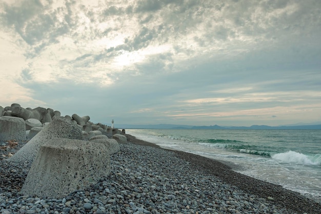 Strand mit Felsbrocken und einem Wellenbrecher im Hintergrund ein Leuchtturm in Fuji City Japan