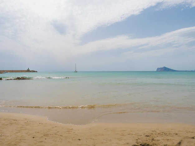 Strand mit Segelboot im Hintergrund und blauem Himmel