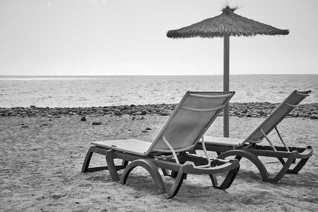 Strand mit Sonnenschirm und Chaiselongues am Meer - Schwarzweißfotografie