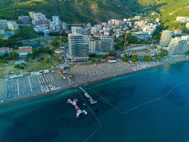 Strand mit Sonnenschirmen, Sonnenliegen und Menschen, die sich in der Stadt Becici in der Nähe der Adria vor dem Hintergrund des sonnigen Himmels entspannen