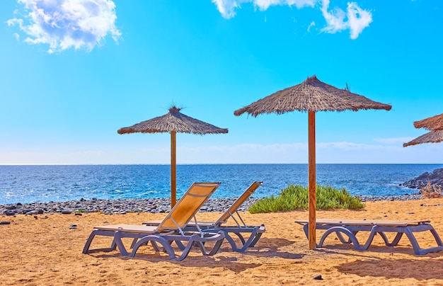 Strand mit Sonnenschirmen und Liegen am Meer an sonnigen Sommertagen