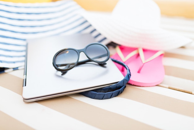 Strand, Sommer, Urlaub, Zubehör und Technologiekonzept - Nahaufnahme von Laptop und Sommerzubehör am Strand