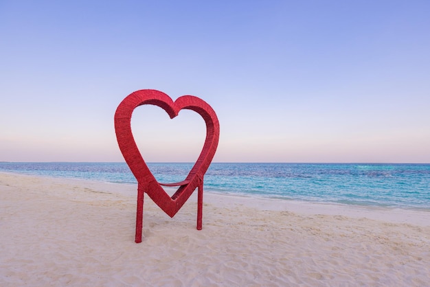 Stranddekoration in Herzform aus Holz. Romantisches Jubiläumskonzept, Liebesbanner mit Sonnenuntergangsfarben