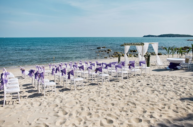 Strandhochzeits-Veranstaltungsort gründete Küste mit weißen chiavari Stühlen mit purpurroter Organzaschärbe