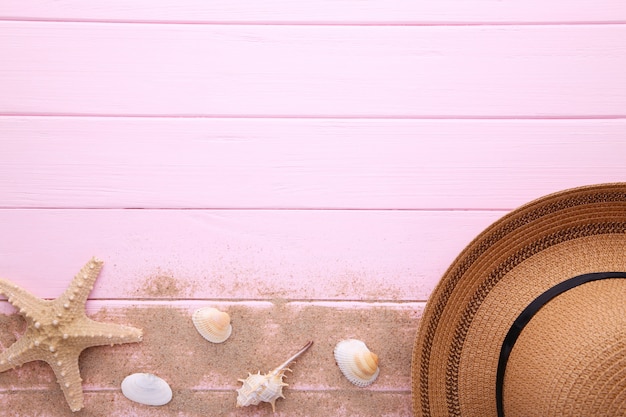 Strandhut mit Muscheln auf rosa Holztisch