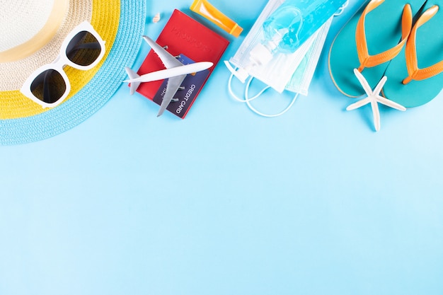 Foto strandhut, sonnenbrille, schutzmaske, händedesinfektionsmittel, reisepass auf hellblauem hintergrund. sommer.