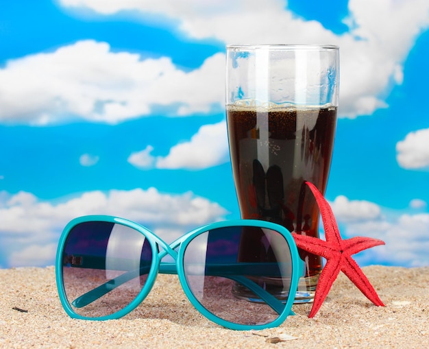 Strandkomposition aus modischer Damensonnenbrille und einem erfrischenden Getränk