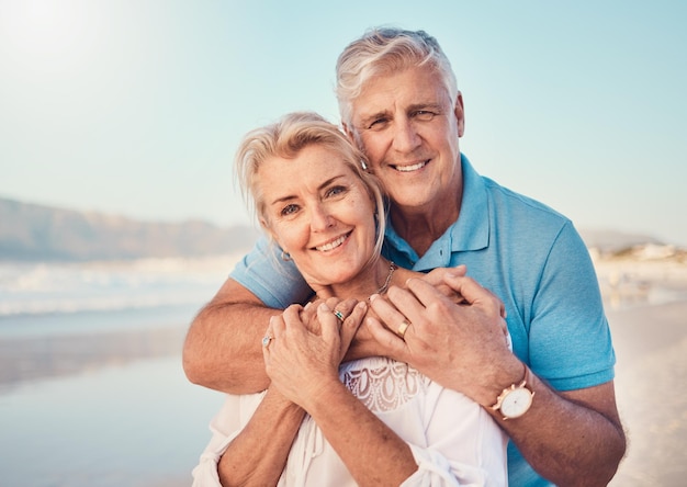 Strandliebe und Porträt eines älteren Paares, das sich im Natururlaub oder bei einem romantischen gemeinsamen Date im Freien am Meer oder am Sand umarmt. Fröhliches Lächeln und Menschen in einer Umarmung, Umarmung oder Glück am Jahrestag