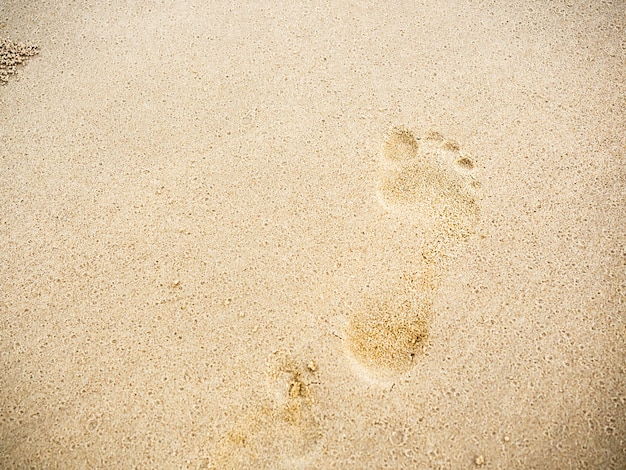 Strandsandabdrücke mit Kopienraum. Schließen Sie den menschlichen Fußabdruck vom Barfußlaufen auf dem Sandstrand-Hintergrund. Reise, Sommerhintergrundkonzept.