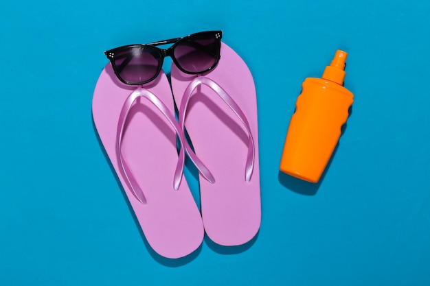 Strandurlaub. Flip-Flops, Sonnencreme-Flasche und Sonnenbrille auf leuchtendem Blau
