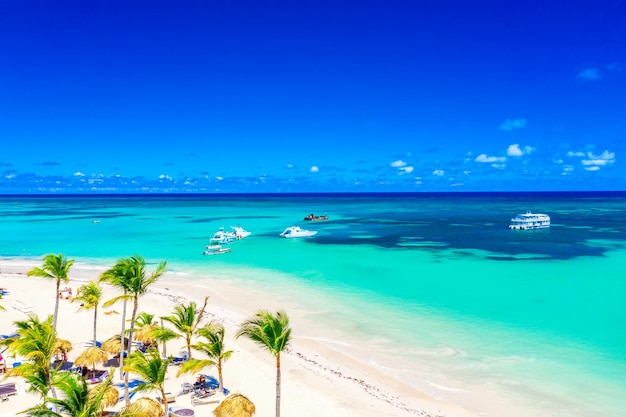 Strandurlaub und Reisehintergrund. Luftdrohne-Blick auf den wunderschönen atlantischen tropischen Strand mit Strohschirmen, Palmen und Booten. Strand von Bavaro, Punta Cana, Dominikanische Republik.