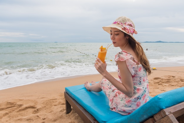 Strandurlaubfrau, die den Orangensaft hat Spaß auf dem Strand trinkt.