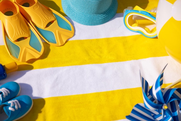 Strandzubehör auf gelb gestreiftem Handtuch Sommerferienkonzept
