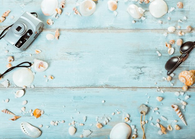 Strandzubehör Sonnenbrille Kamera Muscheln auf blauem Schreibtisch aus Holz Sommerurlaub Hintergrund