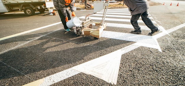 Straßenarbeiter verwenden Anreißmaschinen, um Fußgängerüberwege auf Asphalt in der Stadt zu malen