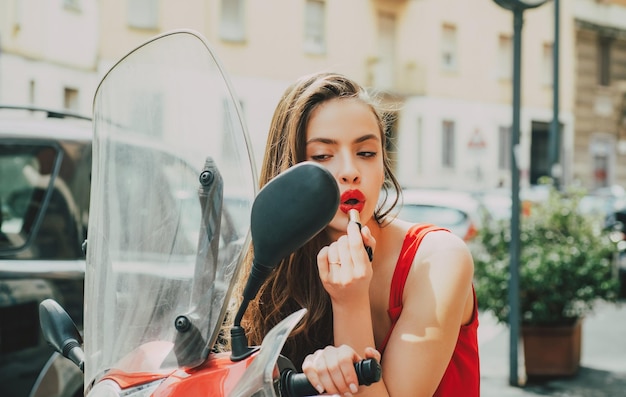 Straßenmake-up sexy Modemädchen mit den roten Lippen legte Lippenstift, der in einen Spiegel des Motorrads schaut