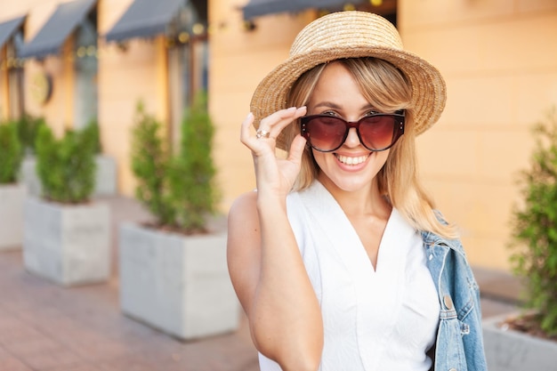 Straßenmode, junge, stilvolle, fröhliche Frau mit Sonnenbrille und Hut in der Stadt