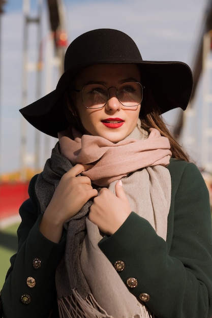 Straßenmodeporträt des attraktiven jungen Modells, das in die Stadt geht. Frau mit modischem Hut, Schal und Brille