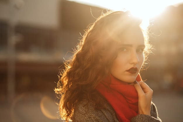 Straßenporträt des eleganten Brunettemodells mit dem gewellten Haar, das in der weichen Abendhintergrundbeleuchtung aufwirft. Platz für Text