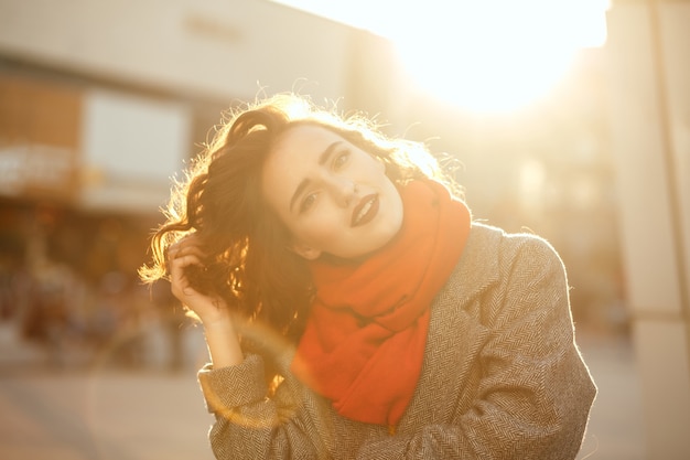 Straßenporträt des romantischen Brunettemodells mit roten Lippen, die mit Sonnenblendung durch die Stadt gehen. Platz für Text