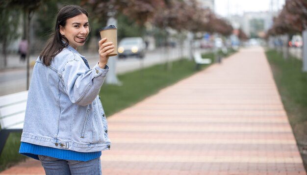 Straßenporträt einer fröhlichen jungen Frau auf einem Spaziergang mit Kaffee auf einem unscharfen Hintergrundkopierraum