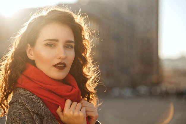 Straßenporträt einer modischen brünetten Frau mit roten Lippen, die am sonnigen Abend durch die Stadt geht. Platz für Text