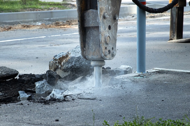 Straßenreparatur. Entfernen einer alten Asphaltschicht mit einem Hydraulikhammer. Wiederaufbau des Bürgersteigs.