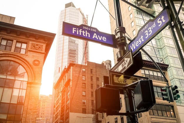 Straßenschild der Fifth Ave und der West 33rd St bei Sonnenuntergang in New York City - Städtisches Konzept und Straßenrichtung in der Innenstadt von Manhattan - amerikanisches weltberühmtes Hauptstadtziel auf warmem, dramatischem, gefiltertem Look