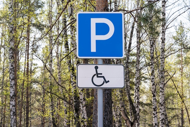 Straßenschild Parkplatz für Behinderte in der Nähe eines Waldes oder öffentlichen Parks, gegen einen Baumtisch