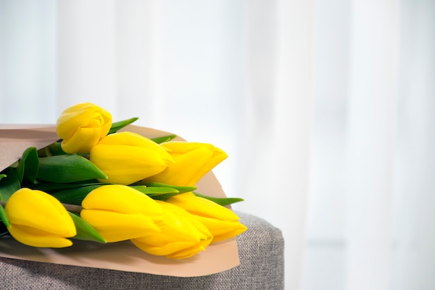 Strauß der gelben Farbe der frischen Tulpen auf grauem Sessel nahe tulled Fenster im Hauptinnenraum