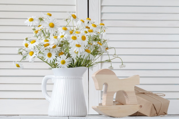 Strauß frischer Gänseblümchen im weißen Krug auf hölzernem Hintergrund