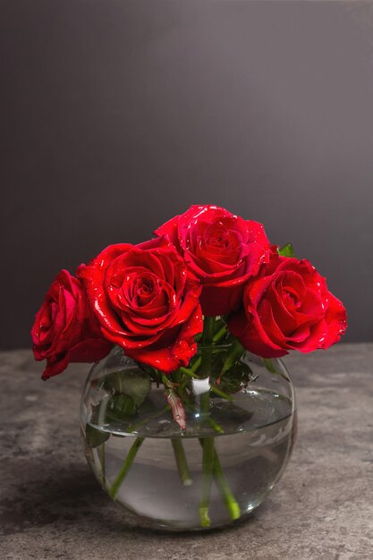 Strauß frischer roter Rosen in einer Vase. Das festliche Konzept für Hochzeiten, Geburtstage, 8. März, Mutter- oder Valentinstag. Grußkarte, dunkler Marmorhintergrund