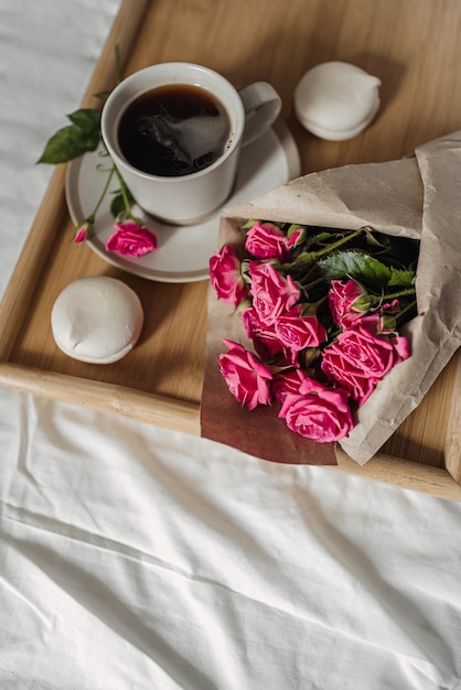 Strauß Frühlingsblumen und eine Tasse Kaffee auf einem Holztablett im Bett