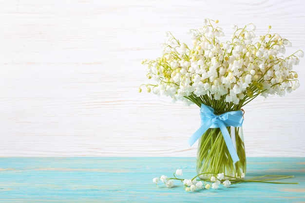 Strauß Maiglöckchen in einer Vase mit blauem Band auf einem blau-weißen Holztisch