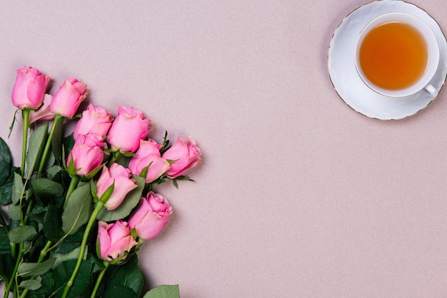 Foto strauß rosa rosen und tasse tee auf rosa hintergrund. flach mit kopierraum liegen.