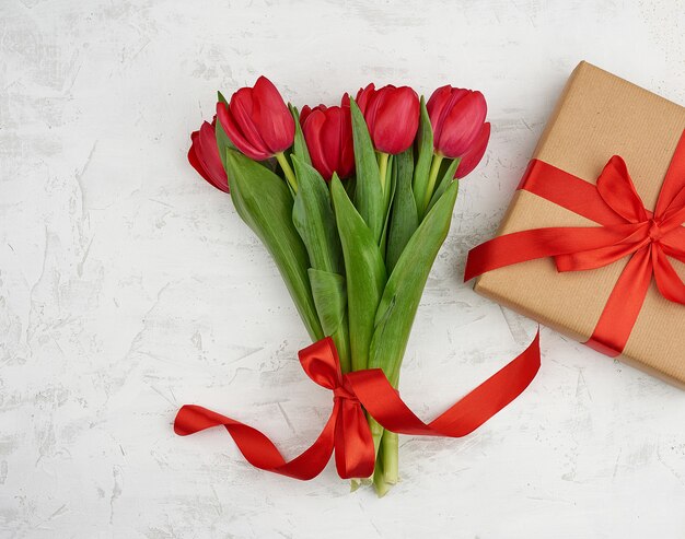 Strauß roter blühender Tulpen mit grünen Blättern, verpacktes Geschenk in braunem Bastelpapier