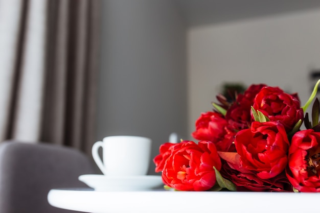 Strauß roter Tulpen auf Tisch und weiße Kaffeetasse. Grußkartenkonzept